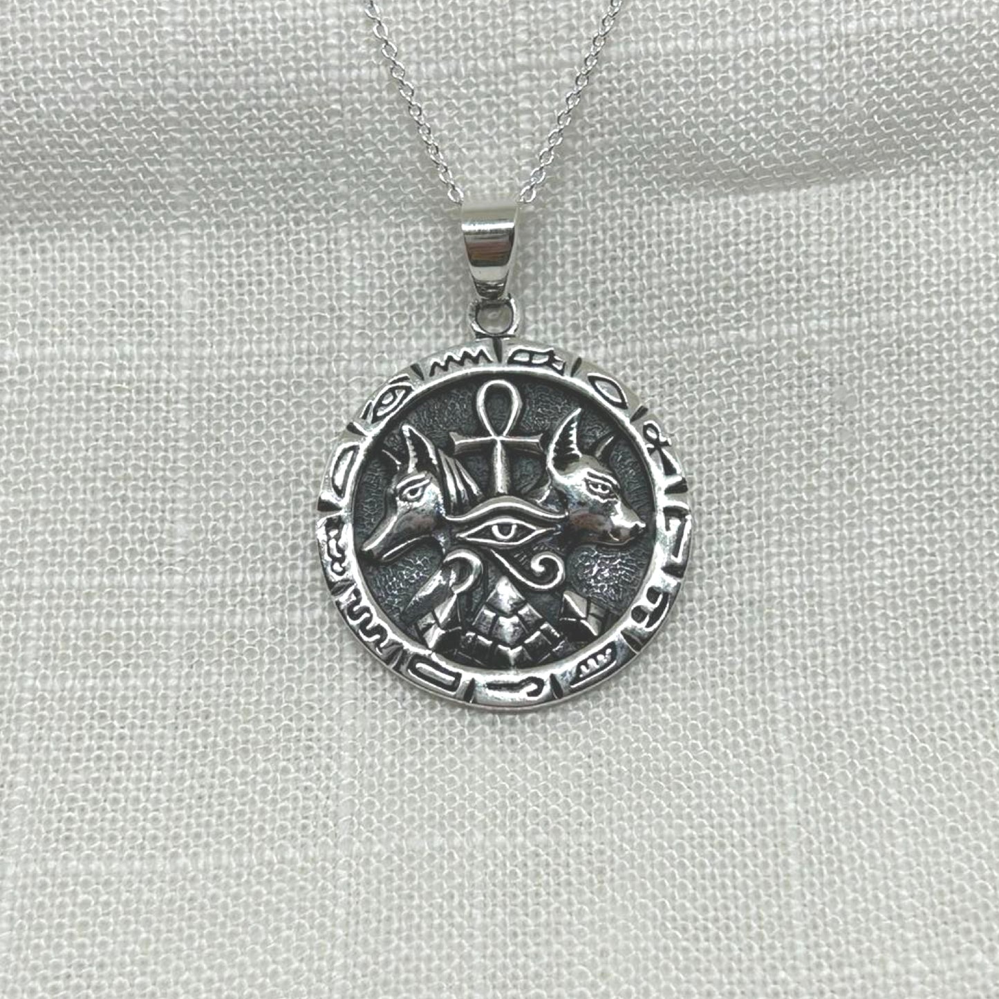 This .925 silver pendant features multiple symbols including an ankh, pyramid, Anubis and eye of Horus.
The oxidized background highlights the intricate details of both symbols, making this necklace a unique and eye-catching accessory.
The pendant is approximately 3.5cm long including the bale x 2.5cm wide x 1mm thick.
The pendant will come on a 20" sterling silver chain and arrive in a tarnish proof bag inside a gift box.