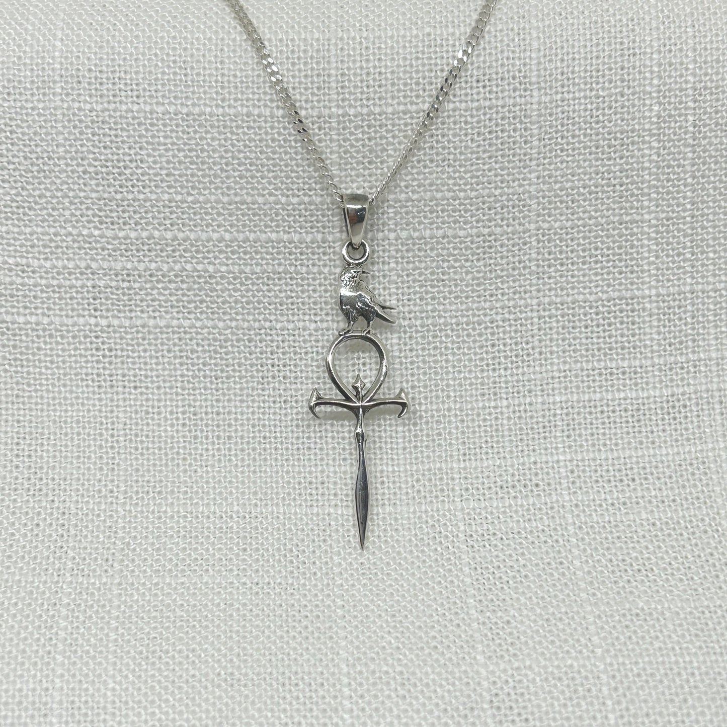 Set in 925 silver this resting raven sits atop a Gothic style sword's hilt. Approximately 4.1cm (inc. bale) x 1.2cm, this highly polished pendant comes supplied on a 20 inch sterling silver curb chain and arrives in a tarnish proof bag inside a gift box.