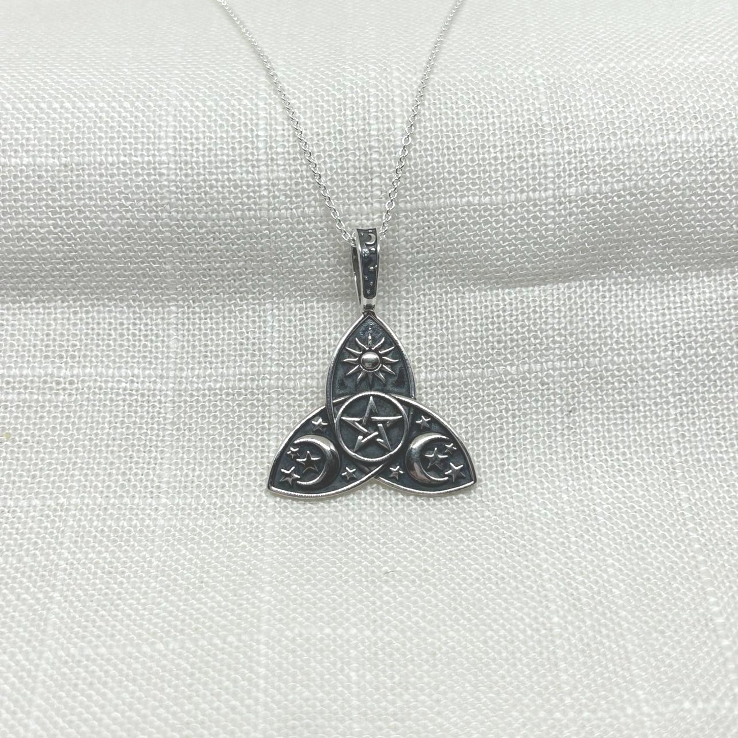 This pendant showcases a triquetra shape in .925 sterling silver, with two crescent moons, stars, a pentagram, and a sun symbol.
The oxidized background highlights the intricate detailing of all the symbols.
The pendant measures 3cm by 2.5cm, including the fixed bale, and comes with a 20 inch silver chain. It is stamped with 925 on the back for authenticity.
The necklace arrives in a tarnish proof bag inside a gift box.