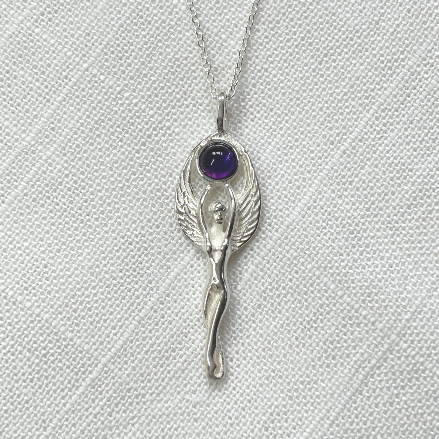 Set in 925 silver, this gorgeous Goddess reaches her arms above her head to hold an amethyst cabochon. Her wings then envelope the outside of the gemstone. She measures 4cm long (inc bale) x 1.3cm wide. All pendants come supplied on a 20" Sterling Silver Curb Chain and are gift boxed. This necklace is also available with a Rainbow Moonstone cabochon.