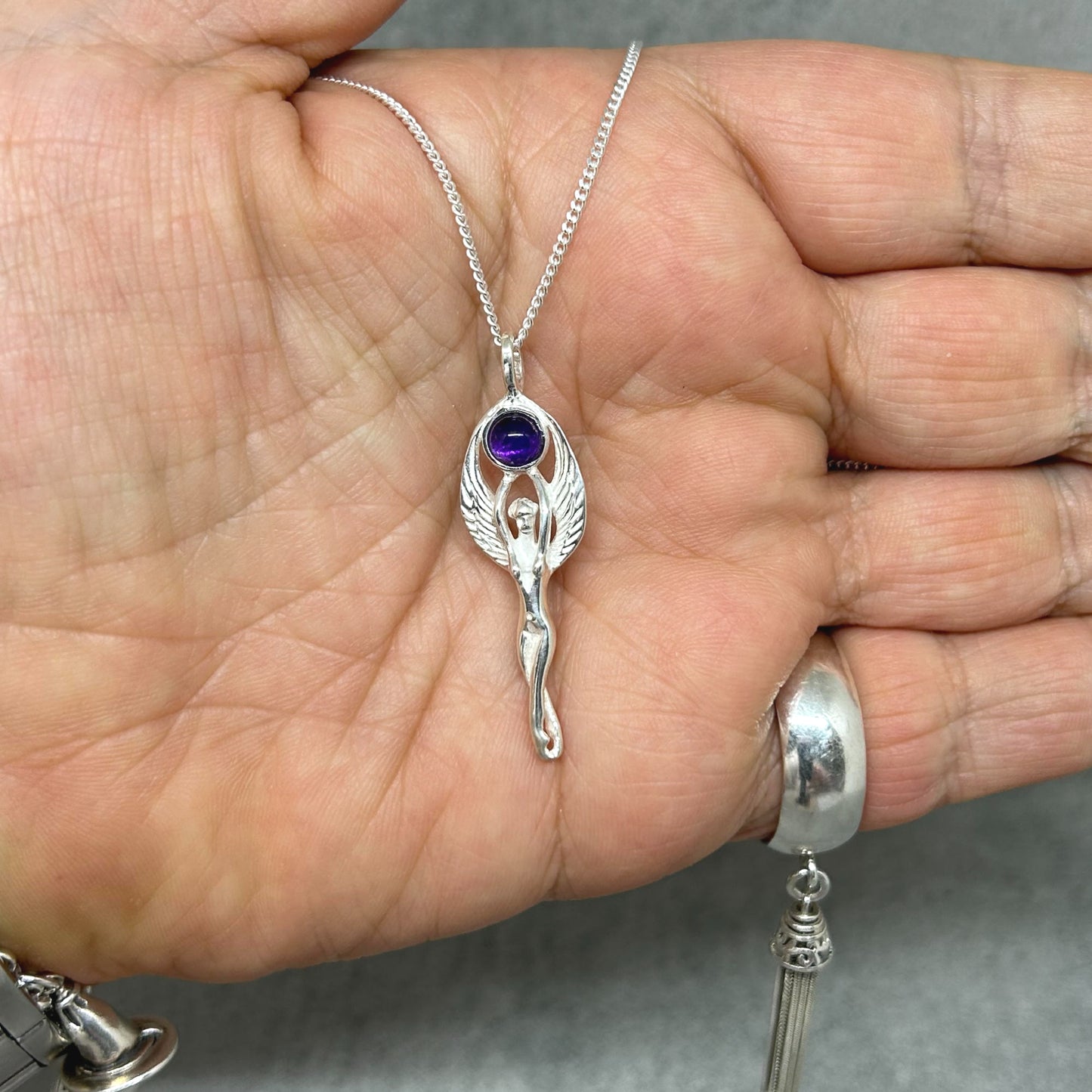Set in 925 silver, this gorgeous Goddess reaches her arms above her head to hold an amethyst cabochon. Her wings then envelope the outside of the gemstone. She measures 4cm long (inc bale) x 1.3cm wide. All pendants come supplied on a 20" Sterling Silver Curb Chain and are gift boxed. This necklace is also available with a Rainbow Moonstone cabochon.