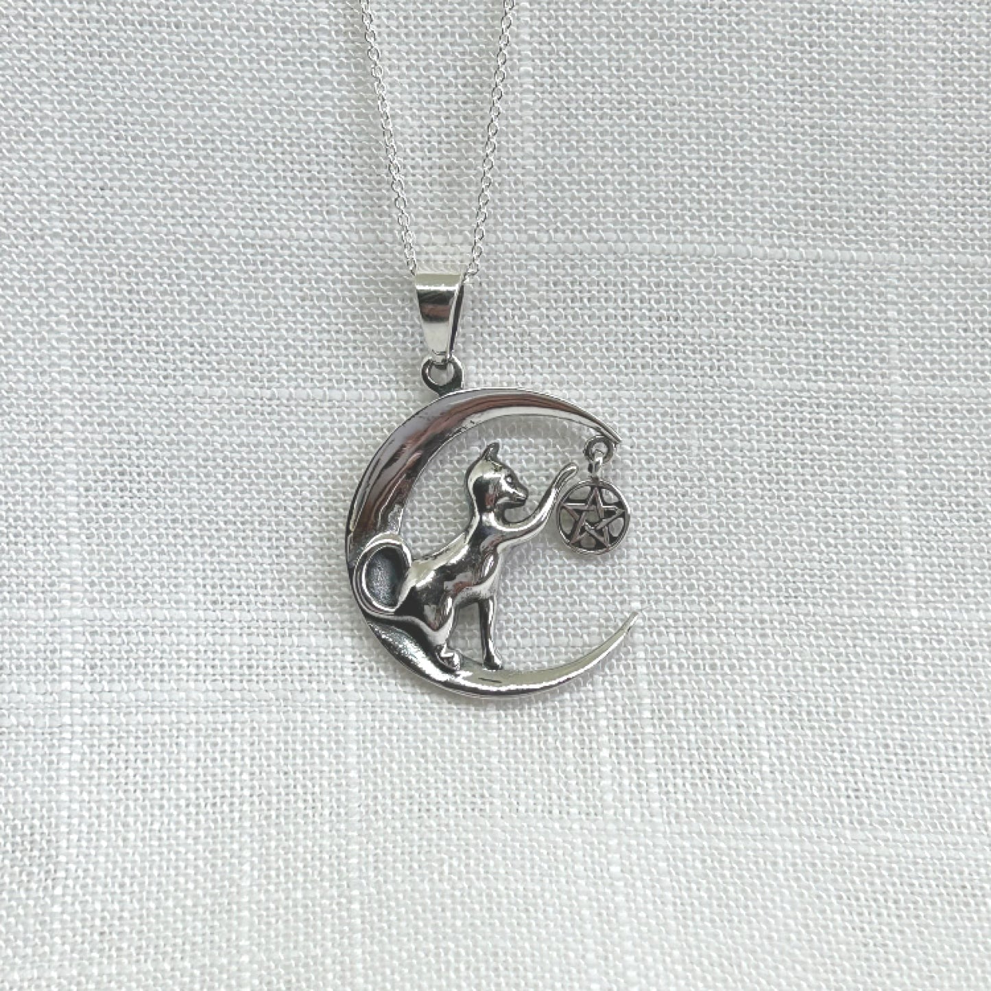 This 925 silver necklace features a cat nestled in a crescent moon, playfully tapping a hanging pentacle and causing it to sway. The pendant measures 3.8cm in height, including the bale by 2.5cm in width. The necklace comes complete with a 20 inch 925 silver chain and is delivered in a tarnish proof bag inside a gift box.