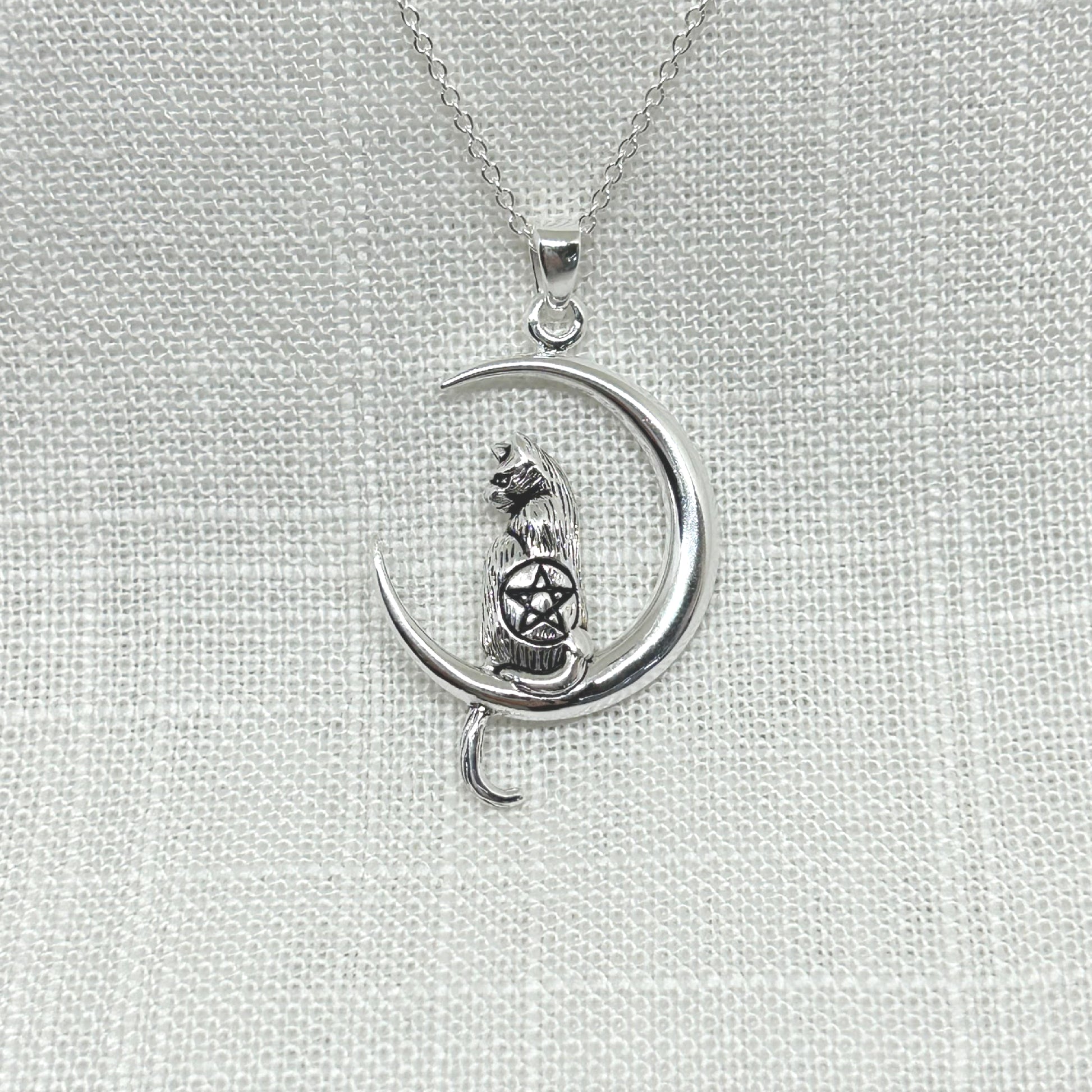 Sitting on a crescent moon is a beautiful 3D Witches' cat, with its head turned to the side and tail hanging below. On the back of the cat is a pentacle symbol. The cat has been slightly oxidised to show off the fur, eyes and ears and pentacle symbol. The pendant is 4cm long including the bale x 2.5cm at its widest.