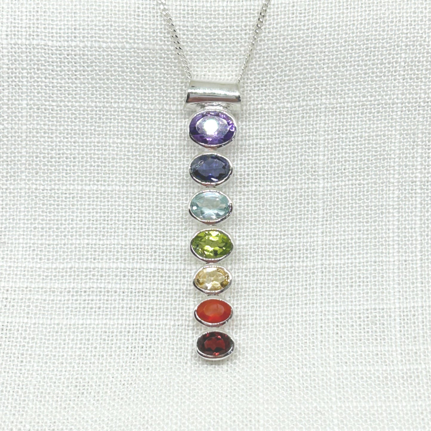 This heavier weight genuine faceted gemstone pendant includes all the essentials of the seven Chakras. These multi coloured gemstones represent the colours of the energy centres within the body know as Chakra points. Amethyst, Iolite, Topaz, Peridot, Citrine, Carnelian, Garnet Size: 5.2cm Long x 1.1cm Wide. Weight is 6.44g All pendants come supplied on a 20 inch sterling silver chain inside a tarnish proof bag and a gift box.