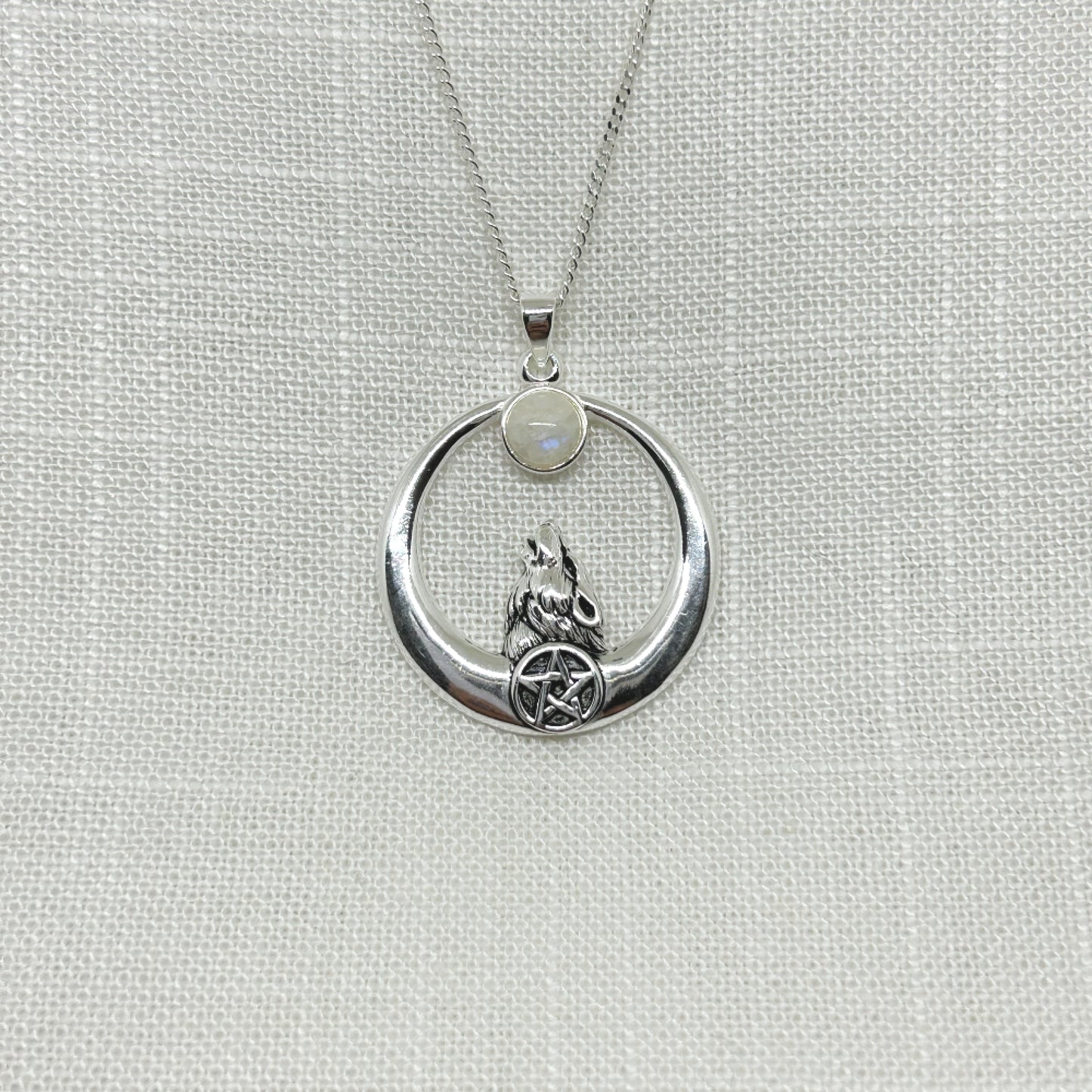 A lone wolf has his head tilted back, gazing up to the full moon, set with a moonstone. Below his neck is a pentacle symbol. Pendant is 3.75cm high and has been slightly oxidized to enhance the detail. It comes complete with a 20 inch silver cable chain.
