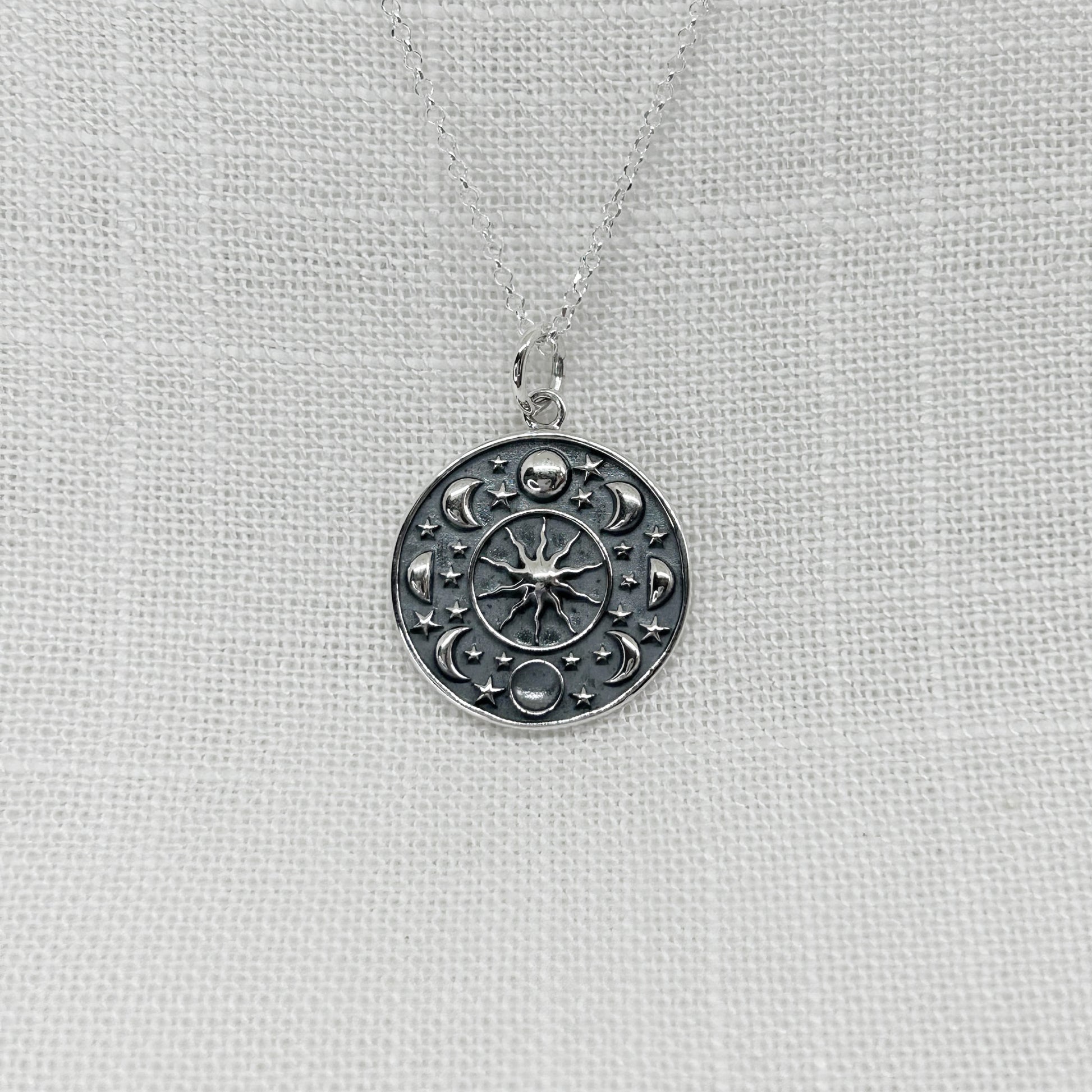 This circular pendant features each phase of the moon and stars. Within the centre, is a sun with its rays shining brightly. A truly cosmic piece! The pendant has a high polish and has been slightly oxidised to show as much detail as possible. The pendant is approximately 2cm in diameter and comes complete on a 20 inch silver chain. All jewellery comes in a tarnish proof bag inside a gift box.