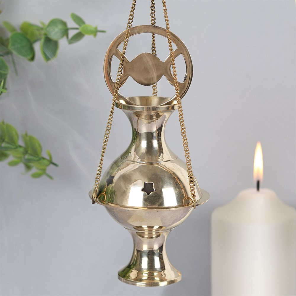 This shiny, brass incense censer features a triple moon symbol, star cut outs on the lid and a convenient chain for hanging. Simply place an incense cone or resin (using a charcoal disc) inside to cleanse the home with its soothing fragrance. Perfect for all your moon rites and rituals! This product is also available with a pentacle design on the top.  Dimensions: H: 27cm tall including chain. x W: 7.5cm x D: 7.5cm  Material: Brass