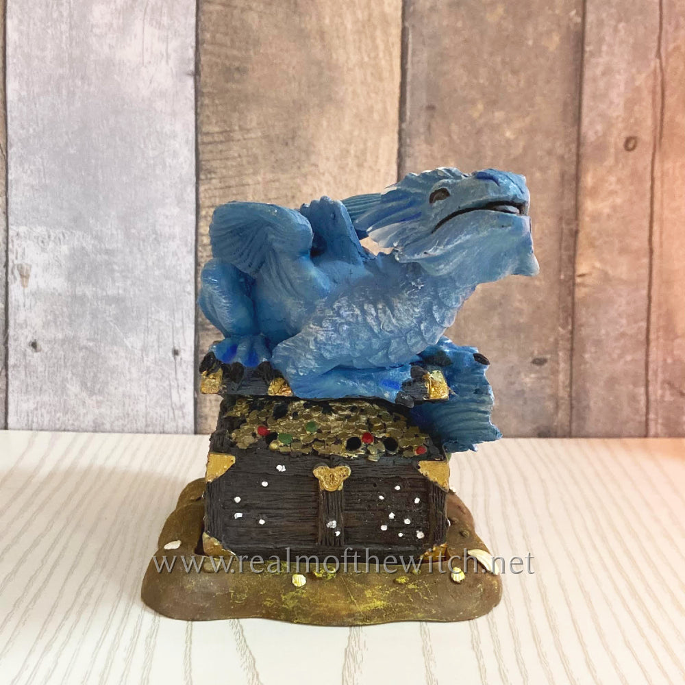 Designed by Anne Stokes. On a sandy beach sits a treasure chest. Atop is a little blue dragon guarding it in this eye-catching incense cone burner. When an incense cone is lit and placed inside the smoke from the cone will flow through the open chest for an impressive feature piece. 