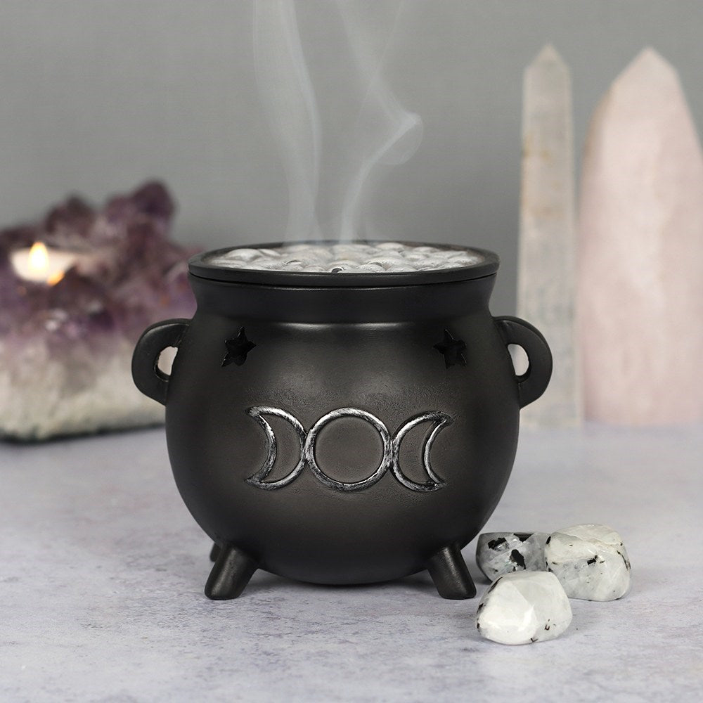 Place your favourite scented incense cones in this magical cauldron, pop the lid on and watch the smoke rise up like a steaming hot brew! Accented by cut out stars and a distressed silver-effect triple moon design, with a removable 'bubbling' brew top. Size: H: 8cm x W: 10cm x D: 9cm